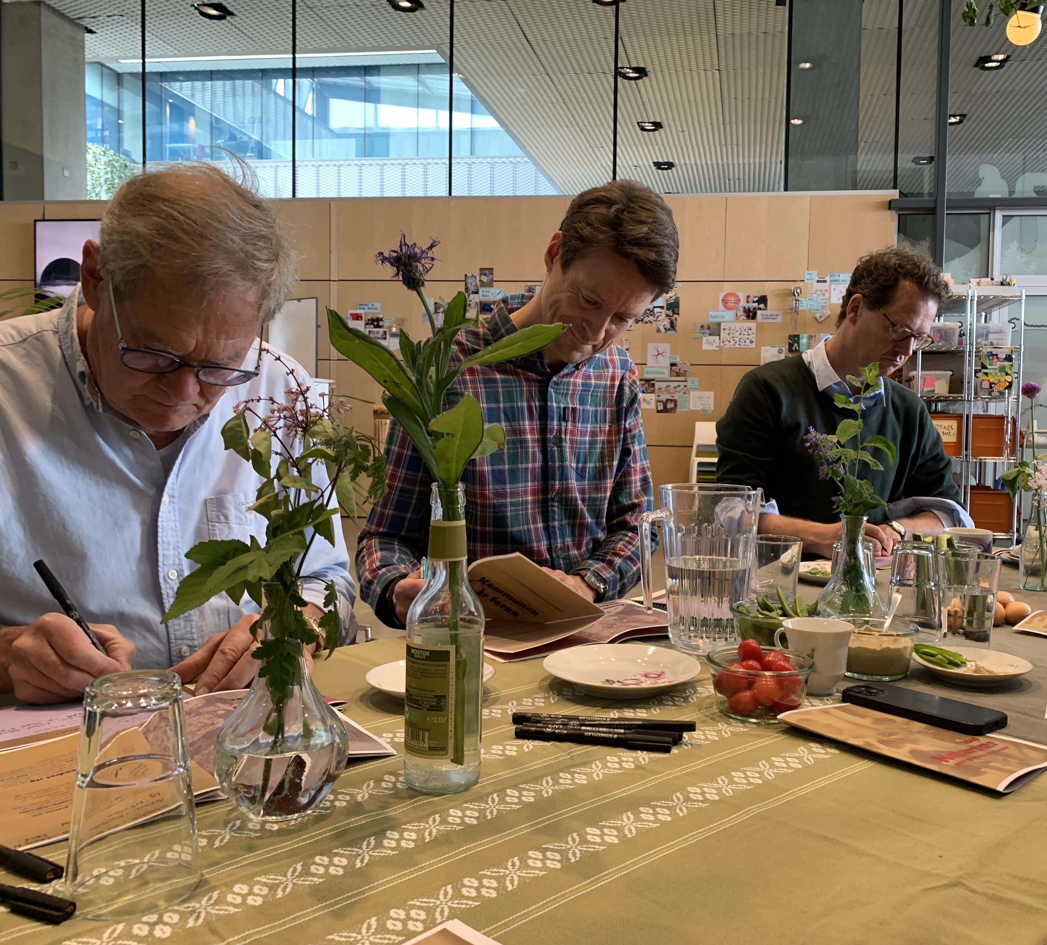 Medlemmer af Klima- og bæredygtighedsudvalget sidder ved et langbord, der er dækket op med vilde blomster, lyskæder og genbrugsporcelæn