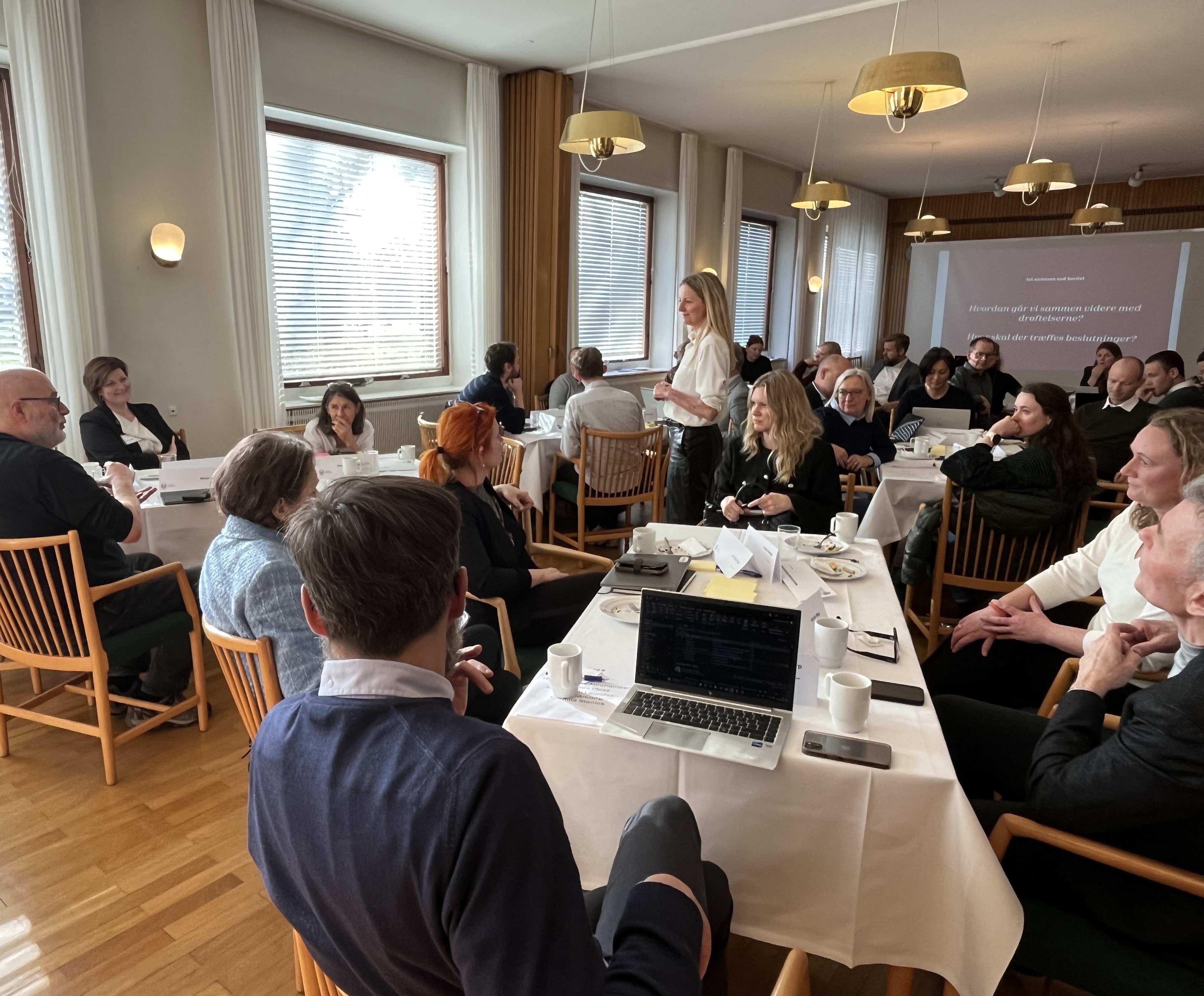 Lokalet fyldt med aktører der lytter til facilitator